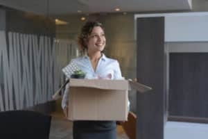 Femme d'affaires heureuse emménageant dans un nouveau bureau et portant ses affaires dans un carton.