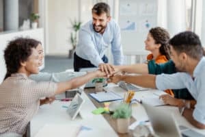 Équipe d’employés divers et heureux joignant leurs mains, célébrant le succès du travail d’équipe et la réussite professionnelle lors d’une réunion, montrant l’unité et le soutien, engagés dans une activité de cohésion d’équipe lors d’un briefing en entreprise.