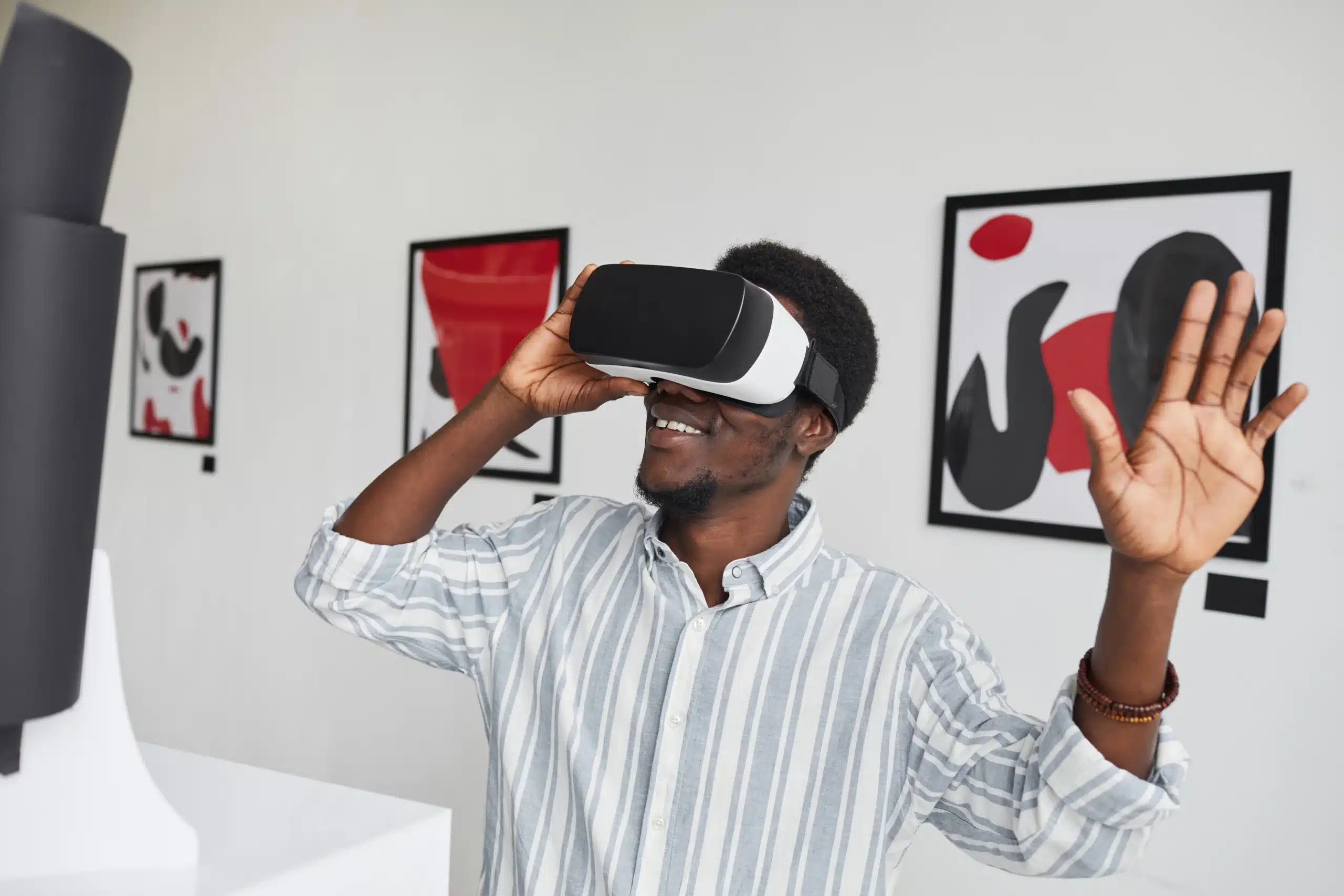 Homme souriant utilisant un casque de réalité virtuelle dans une galerie d'art contemporaine, levant la main avec enthousiasme